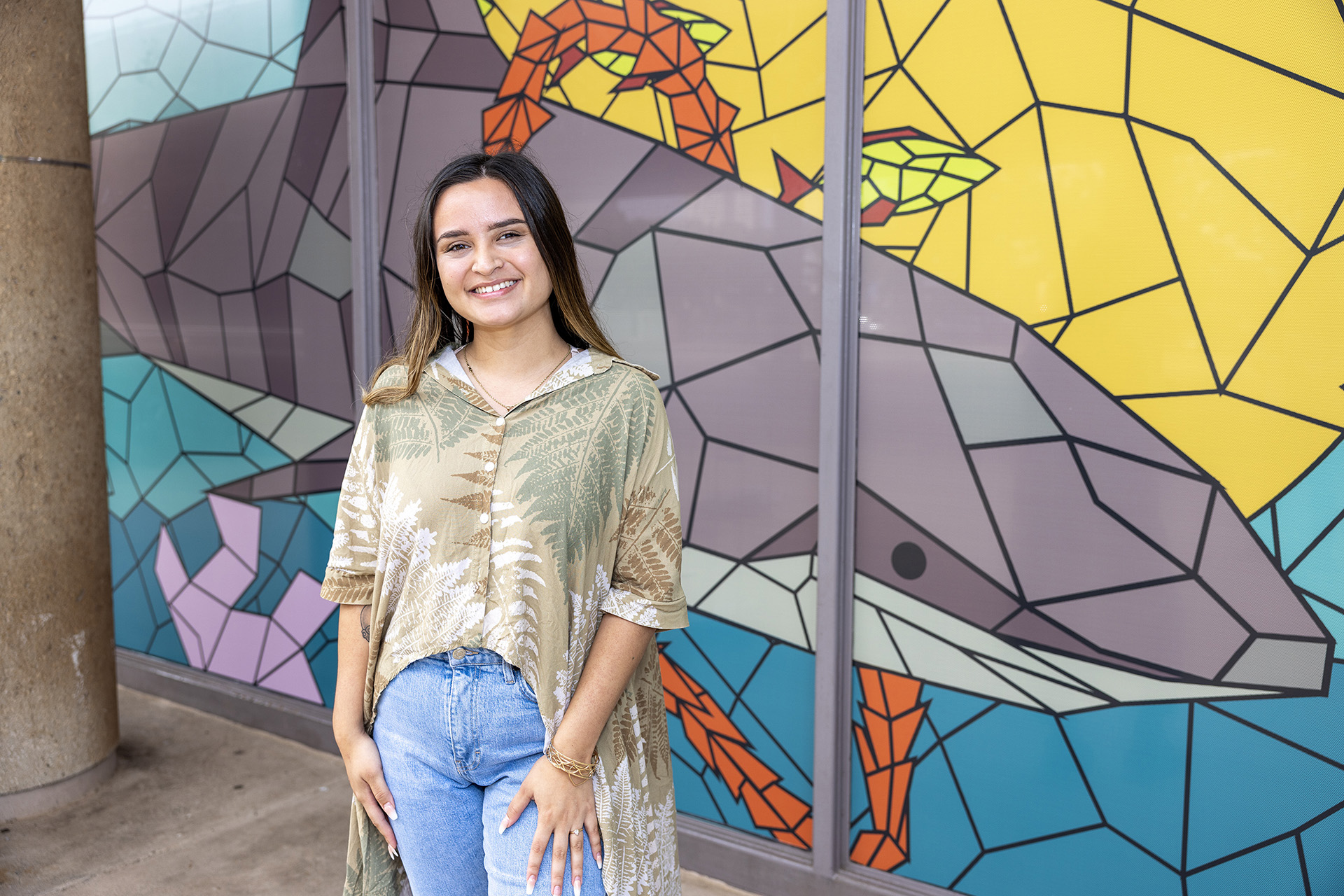 Taylor Wilson in front of her mural at Learning Commons, Nā Kiaʻi o Puʻuloa (The Protectors of Puʻuloa)